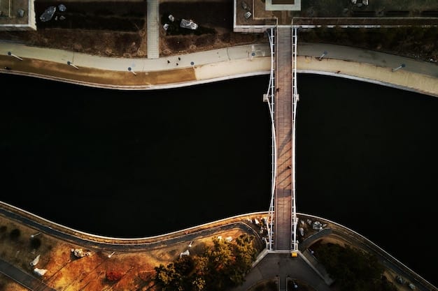 A drone inspecting a bridge. The drone’s camera is pointed at the concrete structure, capturing high-resolution images. Cracks and minor damages are visible on the bridge. The background shows a river flowing underneath the bridge and green trees lining the riverbanks.